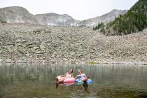 Amigos femininos felizes sentados em anéis infláveis no lago durante as férias — Fotografia de Stock