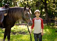 Bonito menino loiro segurando os reinados de cavalo no país. — Fotografia de Stock
