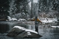 Человек летит рыбачить, стоя в реке зимой — стоковое фото