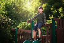 Little boy in camo shirt and shorts sitting at top of a slide. — Stock Photo