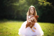 Cute little girl holding a chicken outdoors in backlight. — Stock Photo