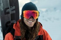 Retrato del hombre sonriente con ropa de abrigo llevando snowboard durante las vacaciones - foto de stock