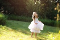 Солодка дівчинка в білій сукні крутиться і танцює на лузі . — стокове фото