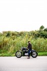 Вид збоку на мотоцикл, що стоїть на дорозі зі своїм власником — стокове фото