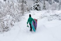 Visão traseira da mulher carregando paddleboard enquanto caminhava no campo de neve — Fotografia de Stock