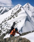 Homem com snowboard escalando rochas na montanha coberta de neve durante as férias — Fotografia de Stock
