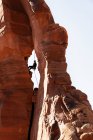 Vista a basso angolo dell'uomo che si arrampica sulle formazioni rocciose contro il cielo limpido al Parco Nazionale Canyonlands — Foto stock