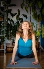 Mujer haciendo yoga en casa plantas de interior en segundo plano - foto de stock