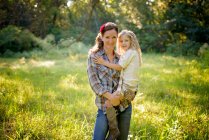 Madre sosteniendo a una niña rubia en un prado en el campo. - foto de stock