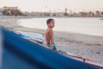 Mignon garçon par le bateau sur la plage — Photo de stock
