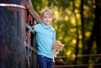 Handsome blond boy holding a kitten outdoors in rural setting. — Stock Photo