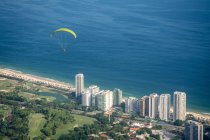 Belle vue sur le parapente survolant les bâtiments résidentiels, les espaces verts et l'océan, vue depuis la rampe de vol libre Pedra Bonita, Tijuca Park, Rio de Janeiro, Brésil — Photo de stock
