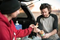 Amigos do sexo masculino tendo comida juntos enquanto sentados no porta-malas do veículo off-road no Parque Nacional de Canyonlands — Fotografia de Stock