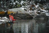 Side view of woman fly fishing while standing in river during winter — Stock Photo
