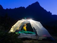 Mujer sentada en carpa iluminada en la montaña por la noche - foto de stock