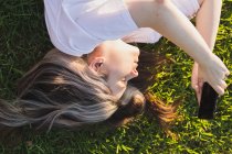 Портрет дівчини, що лежить на траві з телефоном в руках на заході сонця — стокове фото