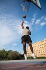 Black man jumping and throwing ball in hoop while playing basketball on street — Foto stock