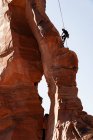 Vue à faible angle de l'homme grimpant sur des formations rocheuses contre un ciel dégagé au parc national des Canyonlands — Photo de stock