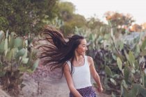 Chica de raza mixta caminando en un sendero de cactus con su pelo largo volando. - foto de stock