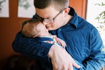 A young father and his newborn son snuggling in their home together — Stock Photo