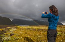 Девушка стоит рядом с озером с радугой перед прекрасным видом на камеру — стоковое фото