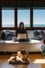 Frau arbeitet mit ihrem Computer in ihrem Strandhaus mit ihrem Hund — Stockfoto