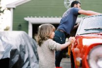 Маленькая девочка моет красную классическую машину вместе со своим отцом — стоковое фото
