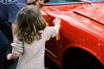 Kleines Mädchen putzt gemeinsam mit ihrem Vater einen roten Oldtimer — Stockfoto