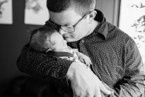 Un padre joven y su hijo recién nacido acurrucados en su casa juntos - foto de stock