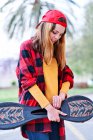 Foto verticale di una giovane ragazza skateboarder in camicia a quadri e berretto rosso guardando giù in città — Foto stock