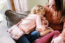 Две девочки и их мать смеются вместе на диване — стоковое фото