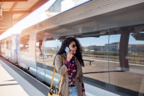 Счастливая молодая афроамериканка разговаривает по мобильному телефону на вокзале в Европе — стоковое фото