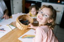 Дитяча дівчинка в окулярах розмальовка зі своєю сім'єю за столом — стокове фото