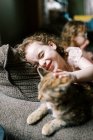 Menina brincando com seu gato no sofá na sala de estar — Fotografia de Stock