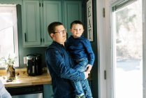 A young boy and his father standing together in kitchen looking out — Stock Photo