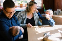 Una giovane famiglia seduta accanto al tavolo da pranzo con neonato e bambino — Foto stock