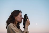 Woman taking pictures outdoor with a film camera during a sunset — Stock Photo