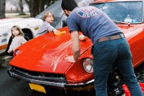Les petits enfants aident leur père à laver une vieille voiture rouge classique à l'extérieur — Photo de stock