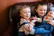 Criança sentada ao lado de seus irmãos em uma cadeira de braço sorrindo — Fotografia de Stock