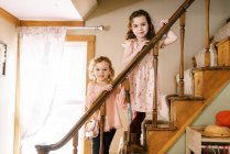 Große und kleine Schwester stehen gemeinsam lächelnd auf einer Holztreppe — Stockfoto
