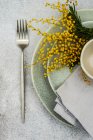 Tischdekoration mit leuchtend gelben Mimosen-Blumen und grauem Geschirr auf Betongrund — Stockfoto