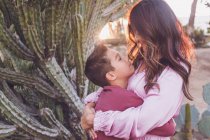 Mother hugging son, both looking at each other with back light sun. — Stock Photo