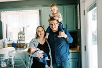 Молодая семья стоит на кухне со своим малышом и новорожденным ребенком — стоковое фото