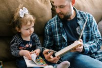 Un padre joven interactuando con su hija y leyendo juntos - foto de stock