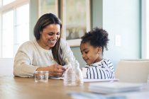 Щаслива мати навчає малювати доньці, сидячи за столом — стокове фото