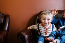 Little toddler sitting next to his siblings on an arm chair smiling — Stock Photo