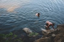 Dos chicos se arrastran a la orilla desde un lago de montaña - foto de stock