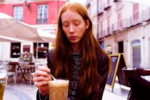 Young red-haired woman drinking coffee on the terrace of a bar — Stock Photo