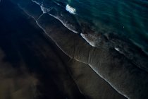 Luftaufnahme von klaren Meereswellen, die mit weißem Schaum an der dunklen, kalten Küste laufen — Stockfoto