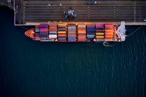 Вид зверху безпілотника завантаженого вантажного корабля з різнокольоровими вантажними контейнерами, пришвартованими на причалі в порту — стокове фото